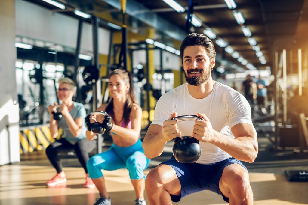 attractive-handsome-bearded-man-holding-kettlebell-doing-squats-fitness-group-with-two-girls-modern-gym.jpg
